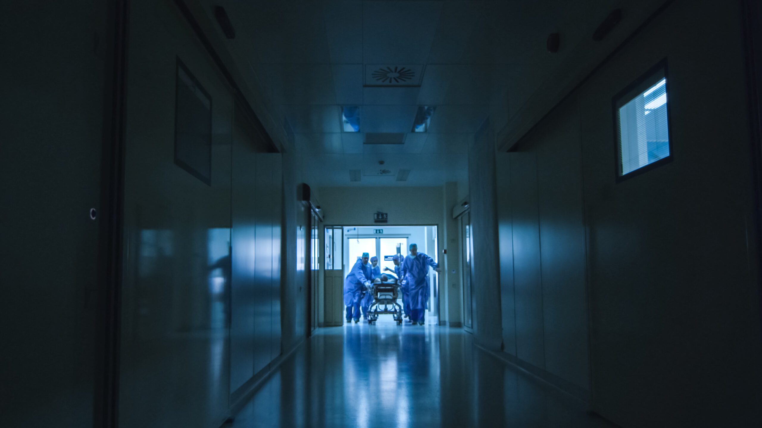Hospital Emergency Team Carrying Stretcher with Patient Through Dark Hospital Hall.